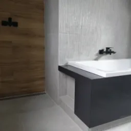 Nowoczesna łazienka z wanną obudowaną czarnym panelem, ściany wyłożone szarymi, prążkowanymi płytkami, drewnopodobna ściana z czarną armaturą.