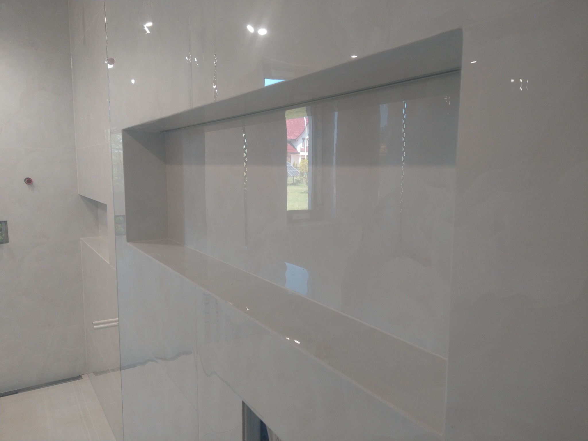 Białe, błyszczące płytki ceramiczne w łazience z wnęką, widok z boku, odbicia światła na powierzchni płytek.