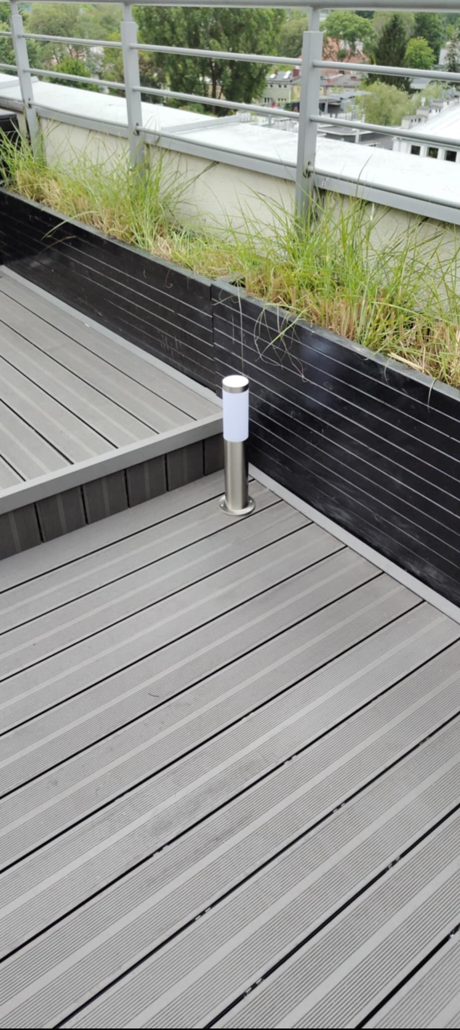 Szary taras kompozytowy z oświetleniem punktowym i donicą z zielenią, widok z góry. Elementy wykończeniowe w kolorze czarnym i srebrnym.