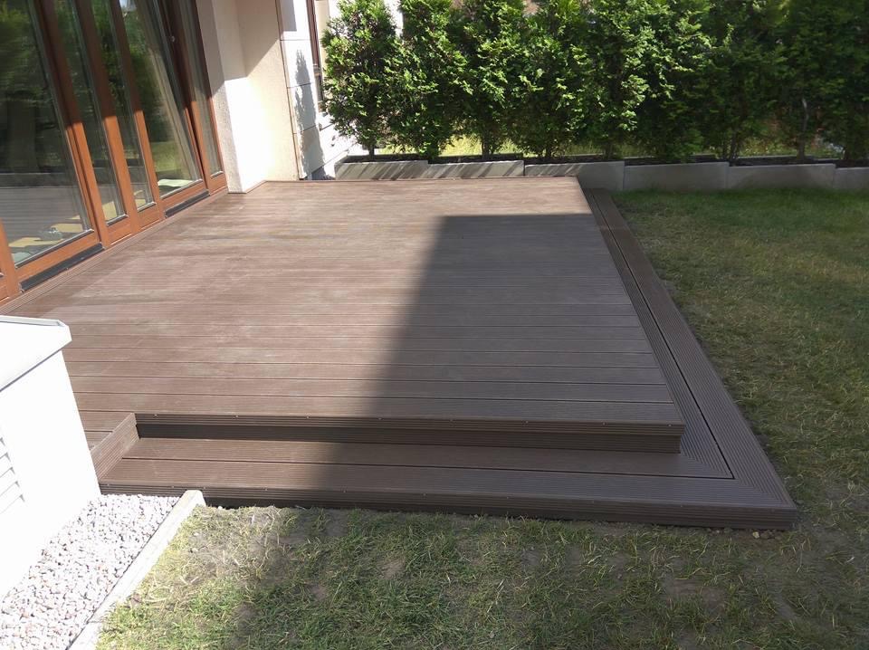 Nowoczesny taras z desek kompozytowych w odcieniach brązu, z niskimi schodami i zielonym trawnikiem w tle. Widoczne detale wykończenia.