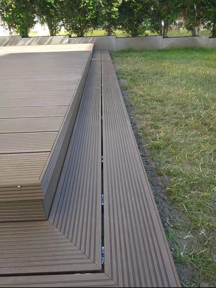 Szczegółowe ujęcie tarasu kompozytowego z widocznymi łączeniami desek i fragmentem trawnika, ukazujące precyzję wykonania i estetykę wykończenia.