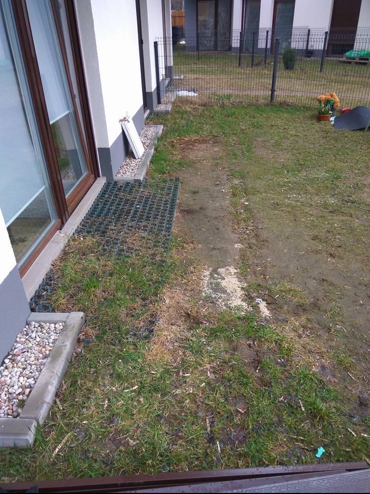 Przygotowanie terenu przy budynku: ułożona krata trawnikowa, obrzeże z kamieni, widoczny fragment trawnika i ogrodzenia. Prace ziemne w toku.