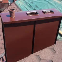 Nowy, brązowy komin z blachy na dachu pokrytym gontem bitumicznym, widoczna membrana dachowa i fragment drabiny.