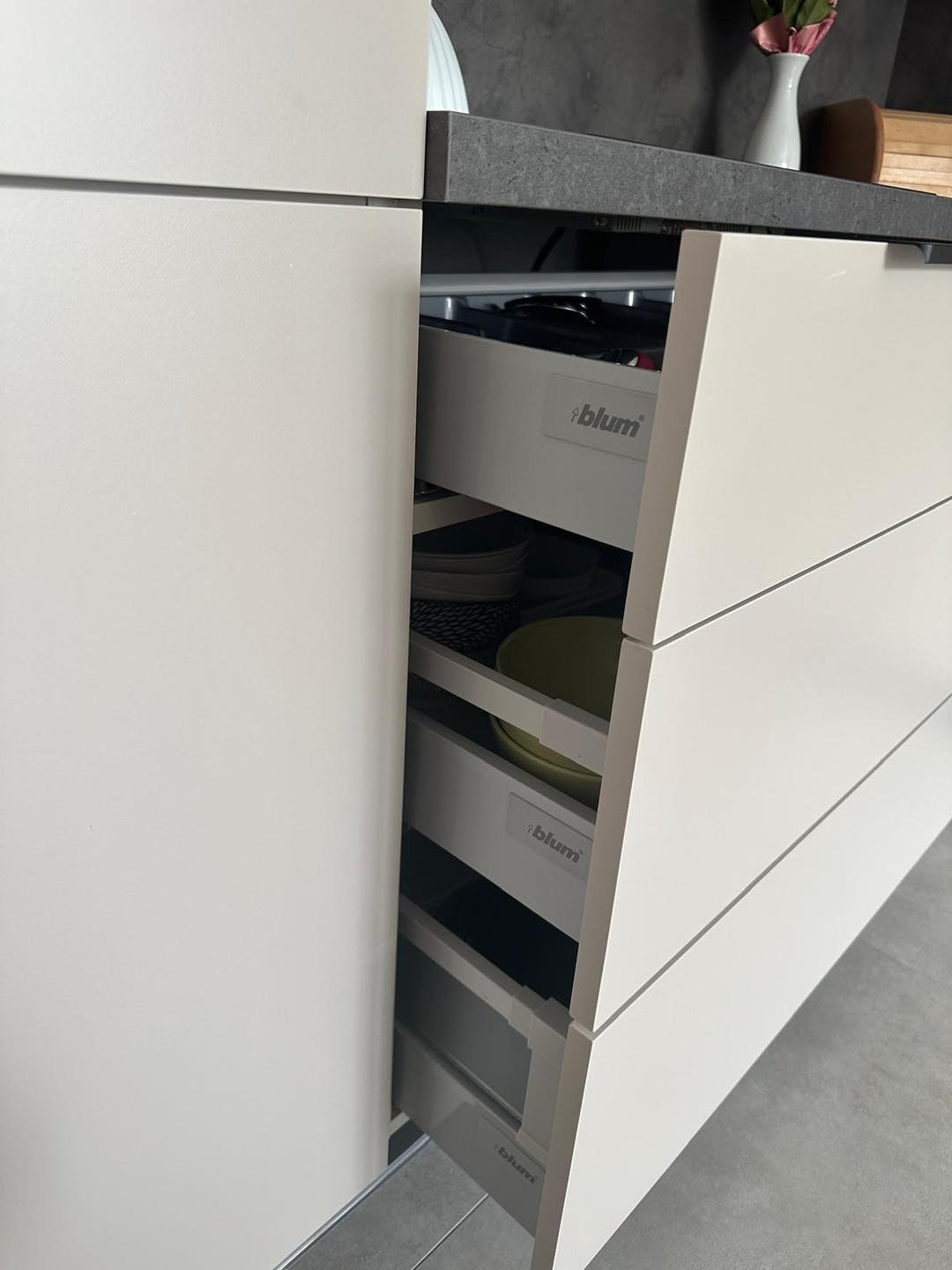 Otwarta szuflada z systemem Blum w zabudowie kuchennej z szarym blatem, widoczne naczynia wewnątrz.