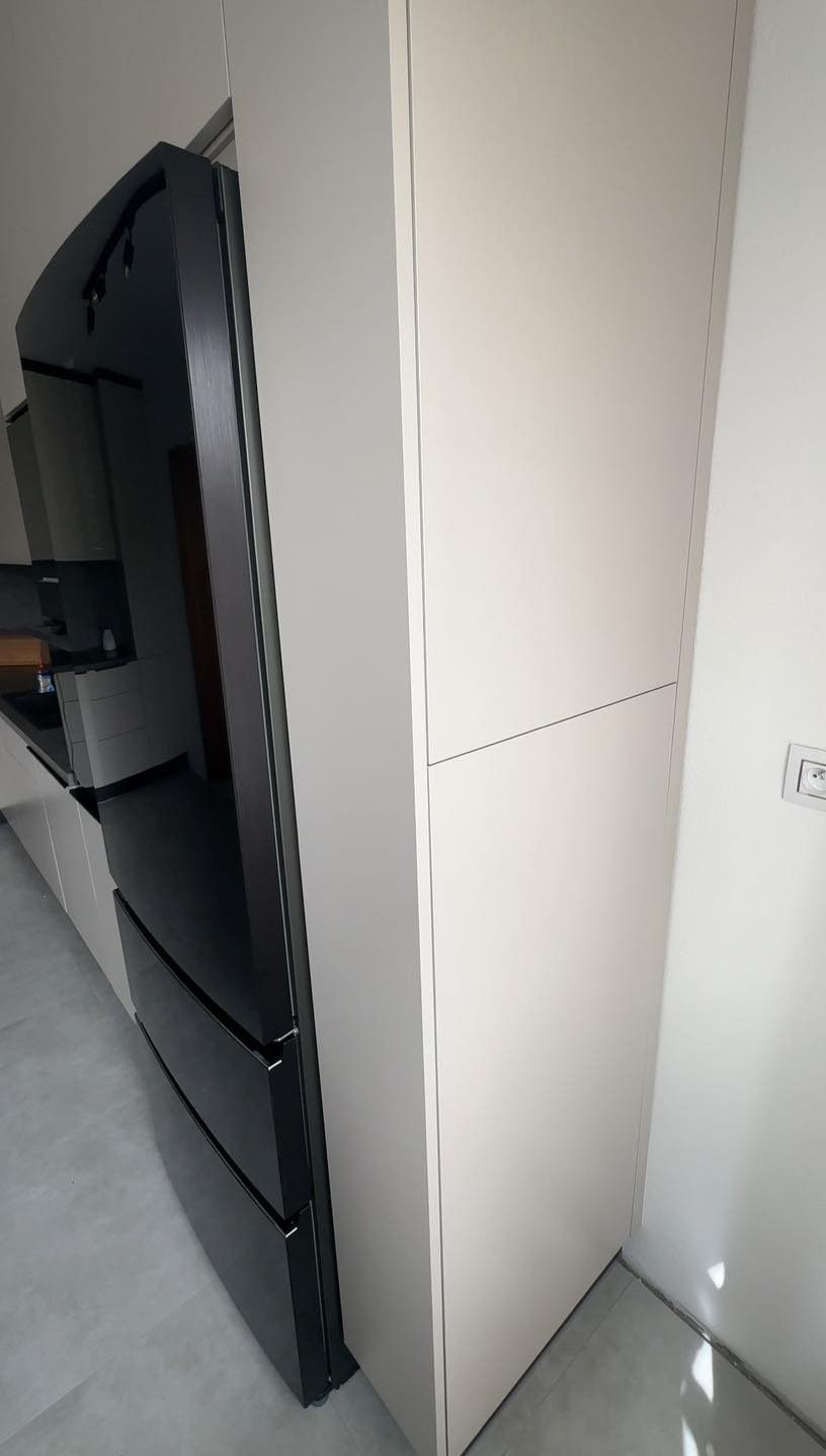 Wbudowana lodówka z czarnym frontem, zintegrowana z jasnymi szafkami kuchennymi na wymiar, widok z boku.