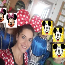 Uśmiechnięta kobieta w stroju Myszki Minnie z dużą, czerwoną kokardą w białe kropki pozuje z grupą dzieci w kostiumach, twarze dzieci zasłonięte grafiką Myszki Miki.