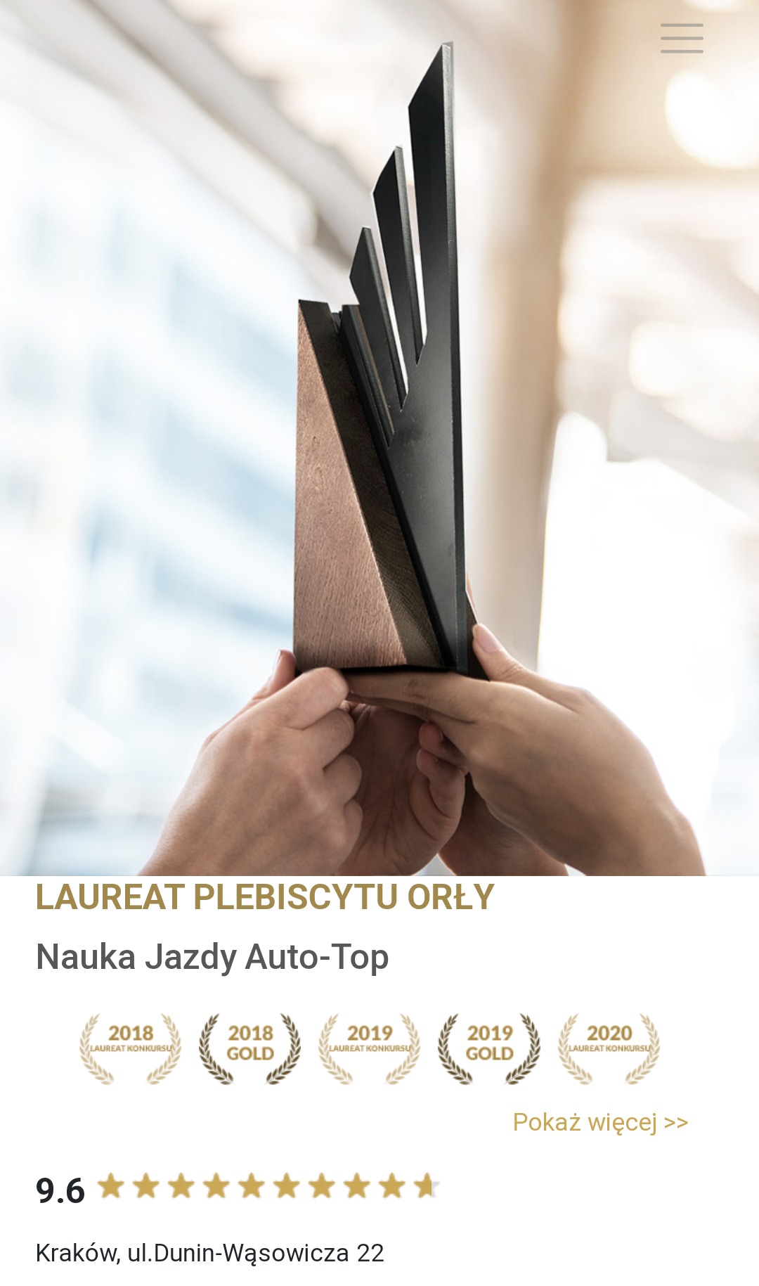 Dłonie trzymające statuetkę nagrody z ciemnego drewna i czarnego metalu, widoczne okno w tle.