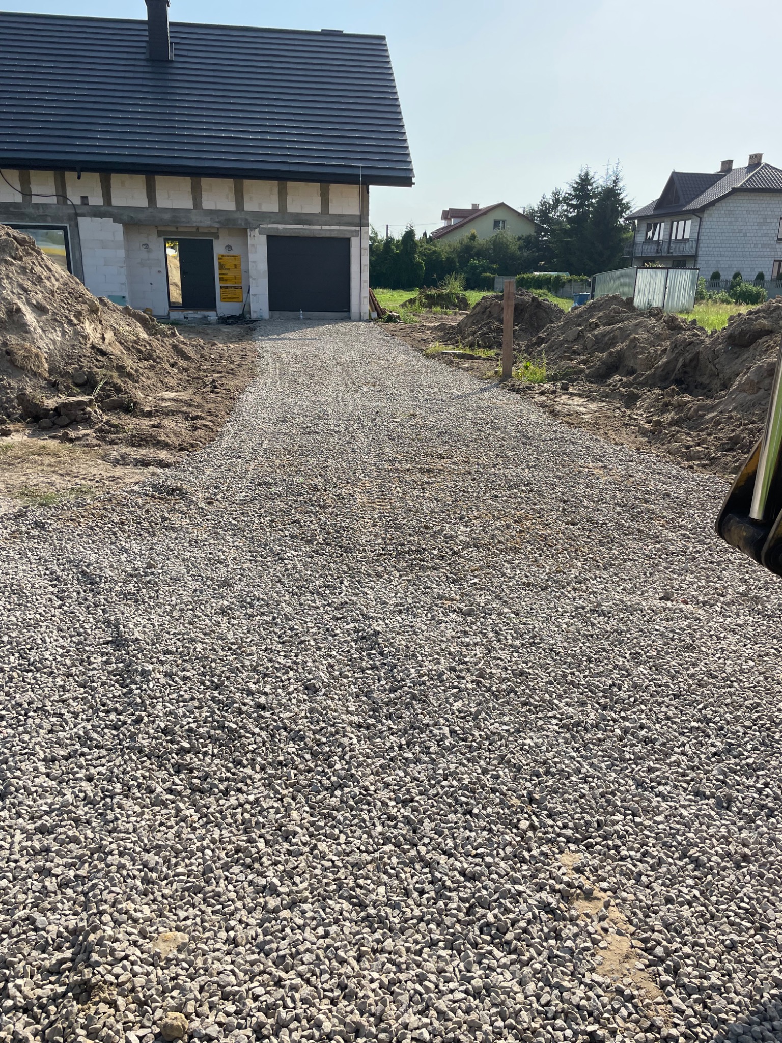 Droga dojazdowa do nowego domu w trakcie budowy, wysypana drobnym, szarym żwirem, obok pryzmy ziemi.