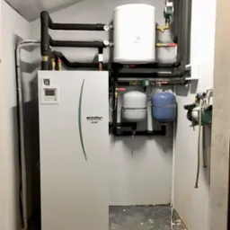 Zainstalowana pompa ciepła marki Mitsubishi Ecodan wraz z osprzętem w kotłowni w G&oacute;rze. Widoczne zbiorniki wyr&oacute;wnawcze, orurowanie i manometry.