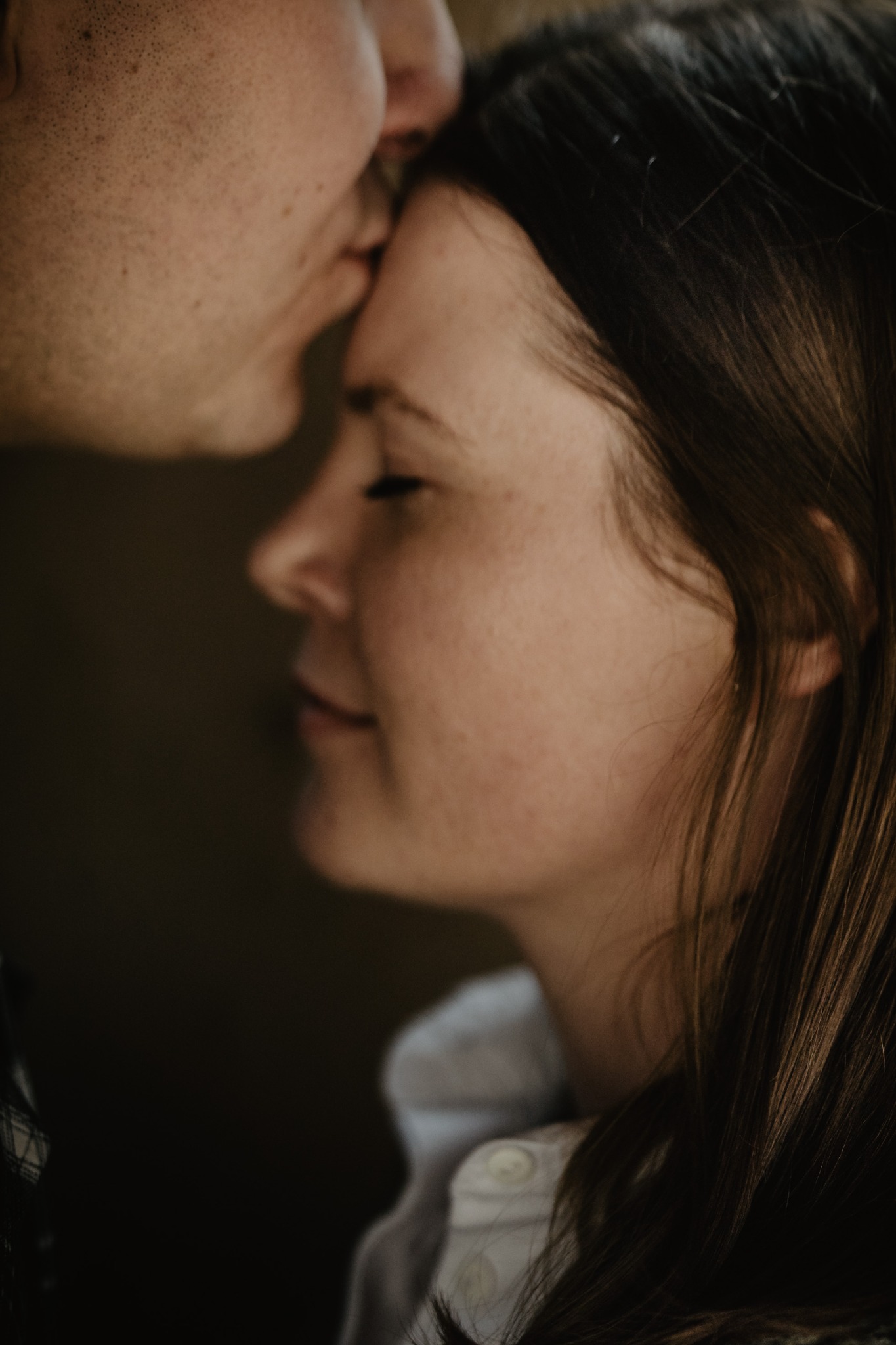 Mężczyzna całuje kobietę w czoło; zbliżenie na profil twarzy kobiety z zamkniętymi oczami.