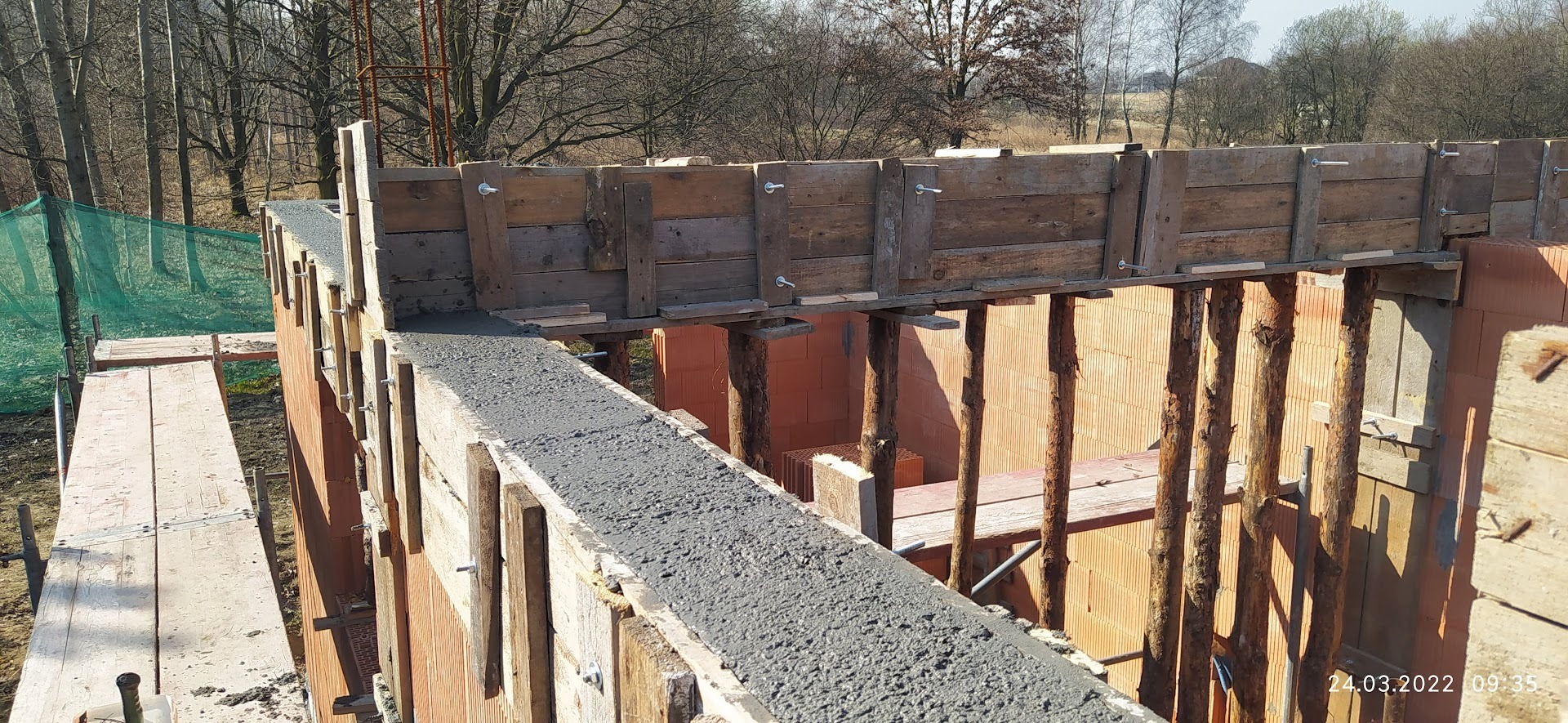 Wieniec betonowy w szalunku z desek na murze z pustaków ceramicznych, wsparty drewnianymi stemplami, widok z góry.