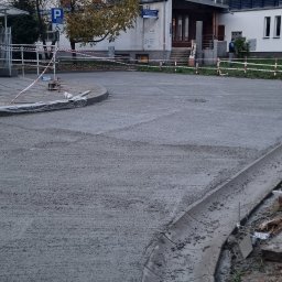 Ivan Polianskyi - Świeżo wylana, szara wylewka na zewnątrz budynku, z widocznymi krawężnikami i taśmą ostrzegawczą. W tle budynki mieszkalne i drzewo z jesiennymi liśćmi.