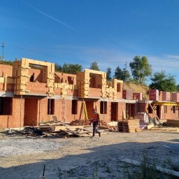 Ivan Polianskyi - Budowa szeregówki z czerwonej cegły w Krakowie, widoczne drewniane szalunki okien i stropów, pracownik w kamizelce odblaskowej na placu budowy.