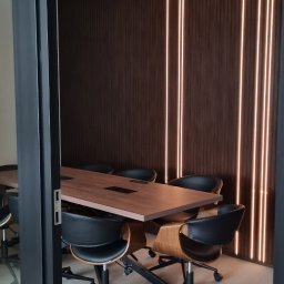 Ivan Polianskyi - Nowoczesna sala konferencyjna z drewnianą ścianą z podświetleniem LED, czarnymi krzesłami i stołem. Widok przez otwarte drzwi, z widocznym fragmentem sufitu.