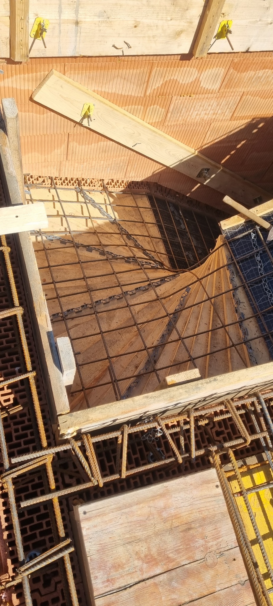 Zbrojenie pod wylewkę schodów z użyciem drewnianych szalunków i cegieł dziurawki. Widoczne pręty zbrojeniowe i elementy konstrukcyjne. Ujęcie z góry.