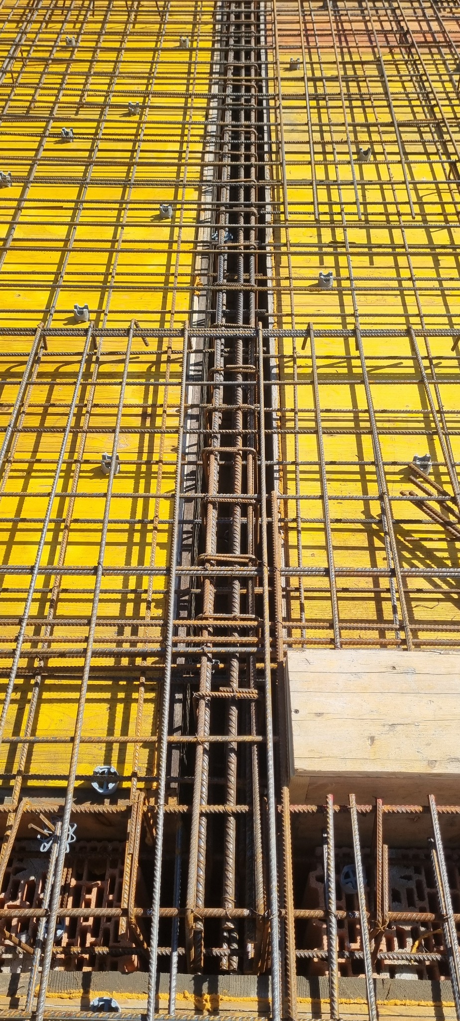 Żółte szalunki zbrojeniowe z widocznymi prętami i strzemionami, przygotowane do wylania betonu. Detal konstrukcji żelbetowej z bliska.