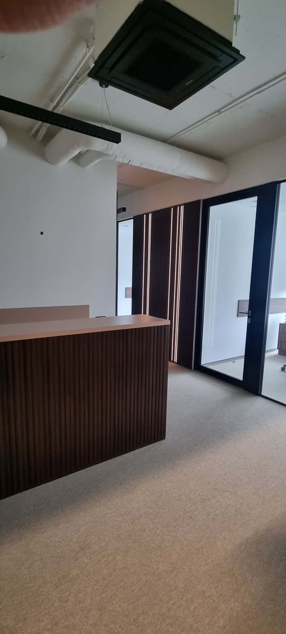 Nowoczesne wnętrze biurowe z recepcją o ryflowanej fakturze, oświetleniem LED i przeszklonymi drzwiami. Minimalistyczny design, stonowana kolorystyka.