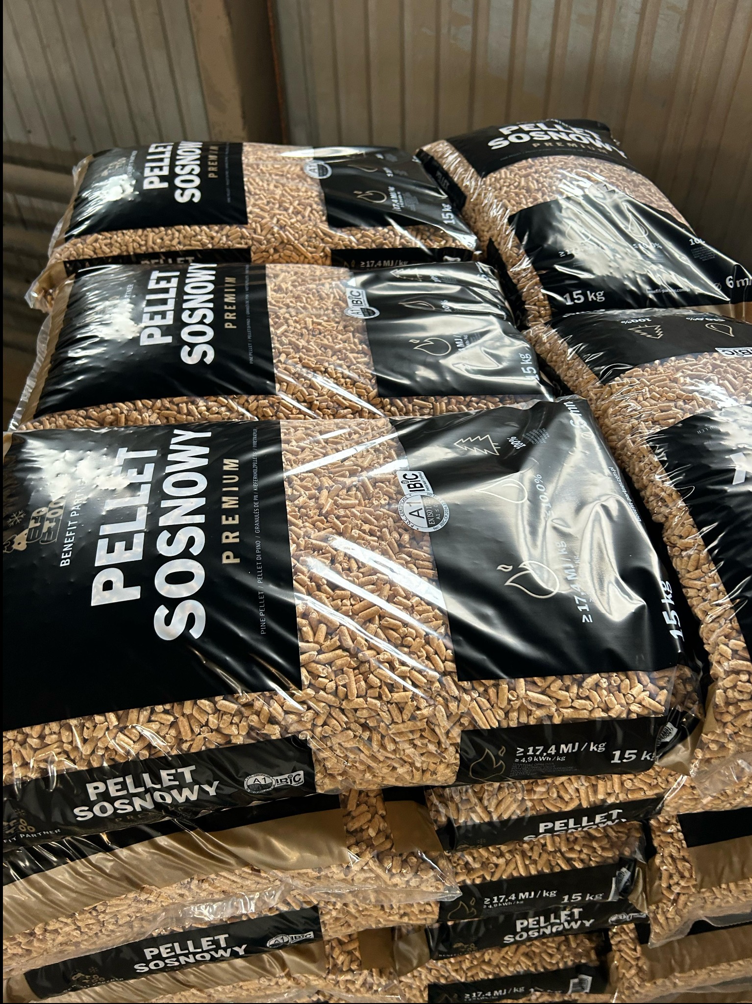Stos worków z pelletem sosnowym premium, każdy o wadze 15 kg, z widocznymi oznaczeniami jakości i certyfikatami. Worki ułożone jeden na drugim, wypełnione jasnymi granulkami pelletu.
