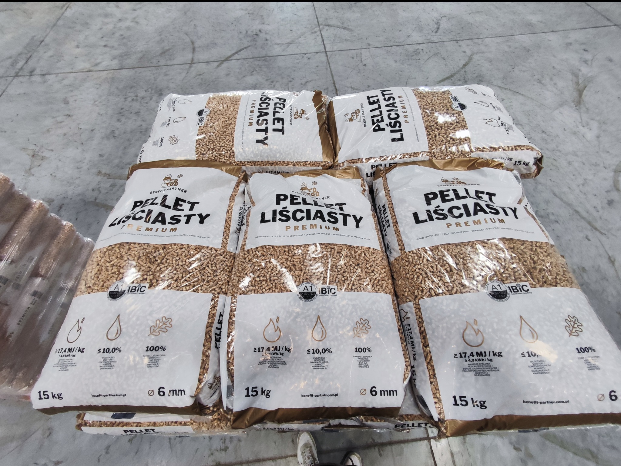 Ułożone worki z pelletem liściastym premium, każdy o wadze 15 kg, z widocznymi specyfikacjami technicznymi i logo producenta na jasnoszarym tle podłogi.