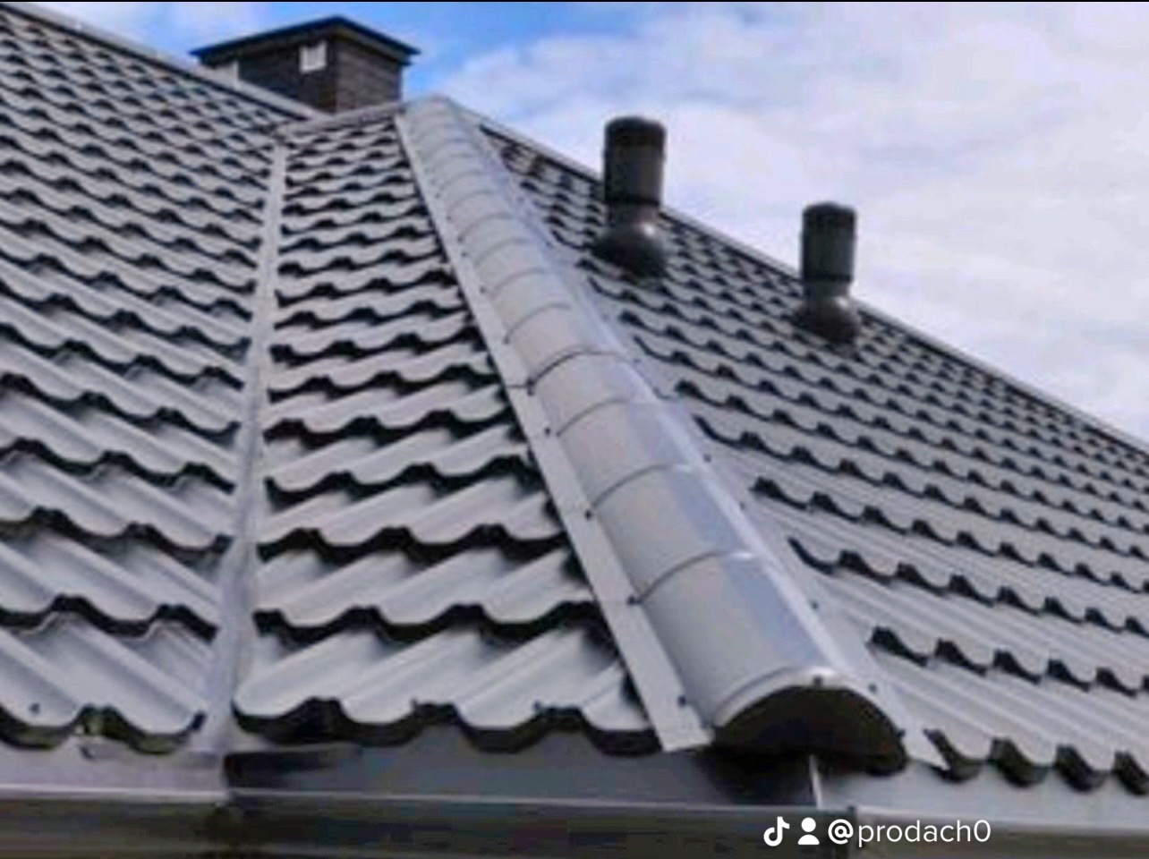 Szary dach z blachy trapezowej z kominkami wentylacyjnymi i obróbką blacharską na kalenicy, widok z dołu.