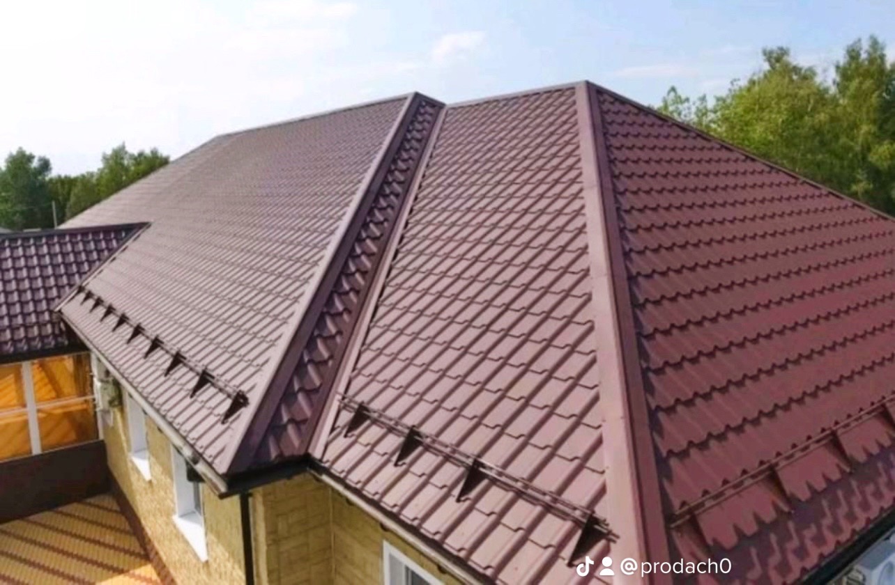 Brązowy dach z blachodachówki modułowej, widok z góry na dom z żółtą elewacją i zielonymi drzewami w tle.