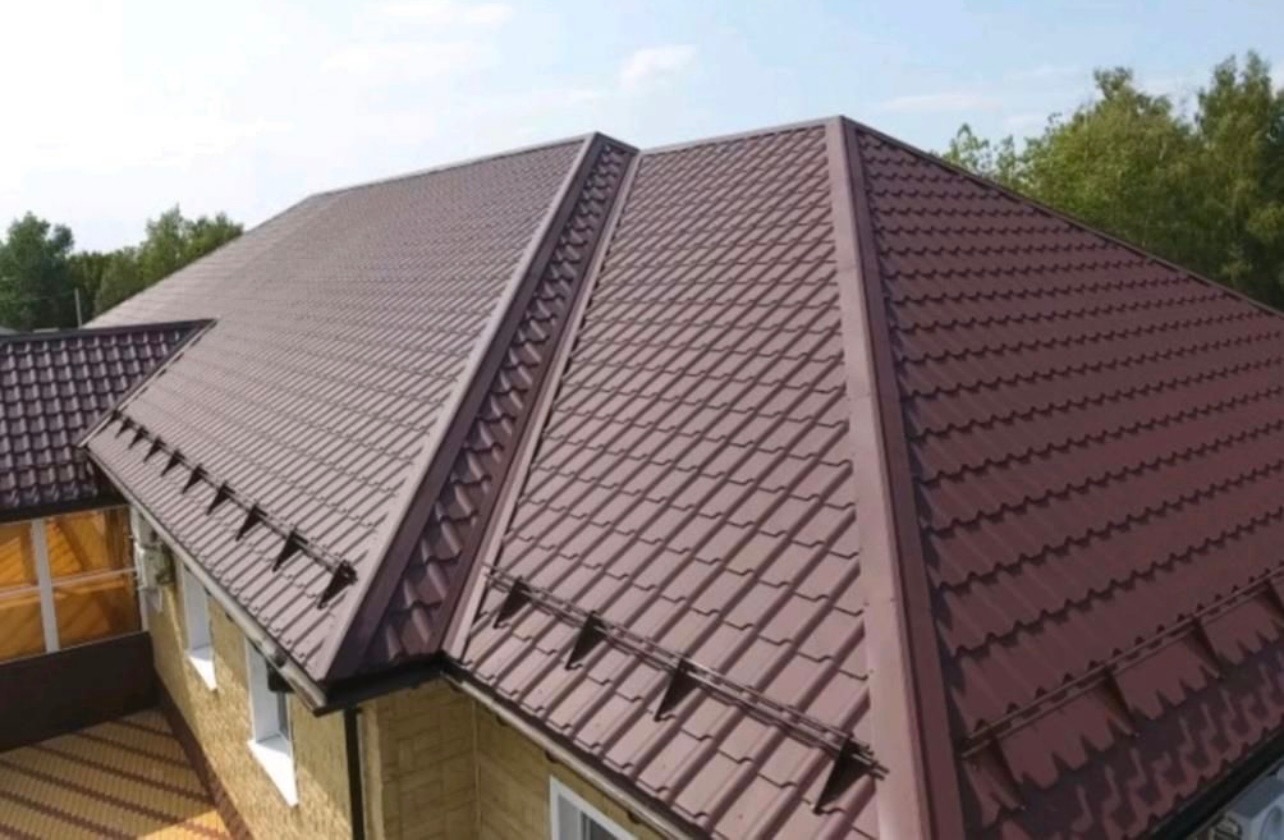 Brązowy dach z blachy trapezowej, widok z góry, z elementami zabezpieczającymi przed zsuwaniem się śniegu, na tle zielonych drzew.