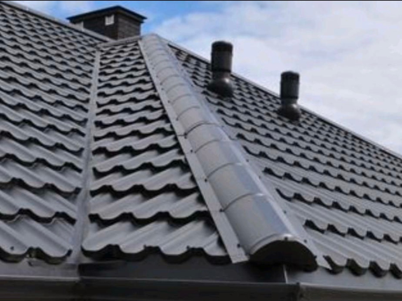 Szary dach z blachodachówki z kominkami wentylacyjnymi i zabezpieczeniem przeciwśniegowym wzdłuż kalenicy.