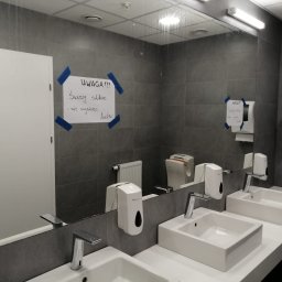 UPGRADE IVAN BOICHUK - Publiczna toaleta z dwoma umywalkami, szarą glazurą i lustrem z kartką 'Uwaga! Świeży silikon - nie wycierać luster.'