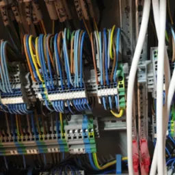 Panel elektryczny z uporządkowanymi przewodami w różnych kolorach, podłączonymi do listew zaciskowych z numerowanymi etykietami, widoczne szyny DIN.