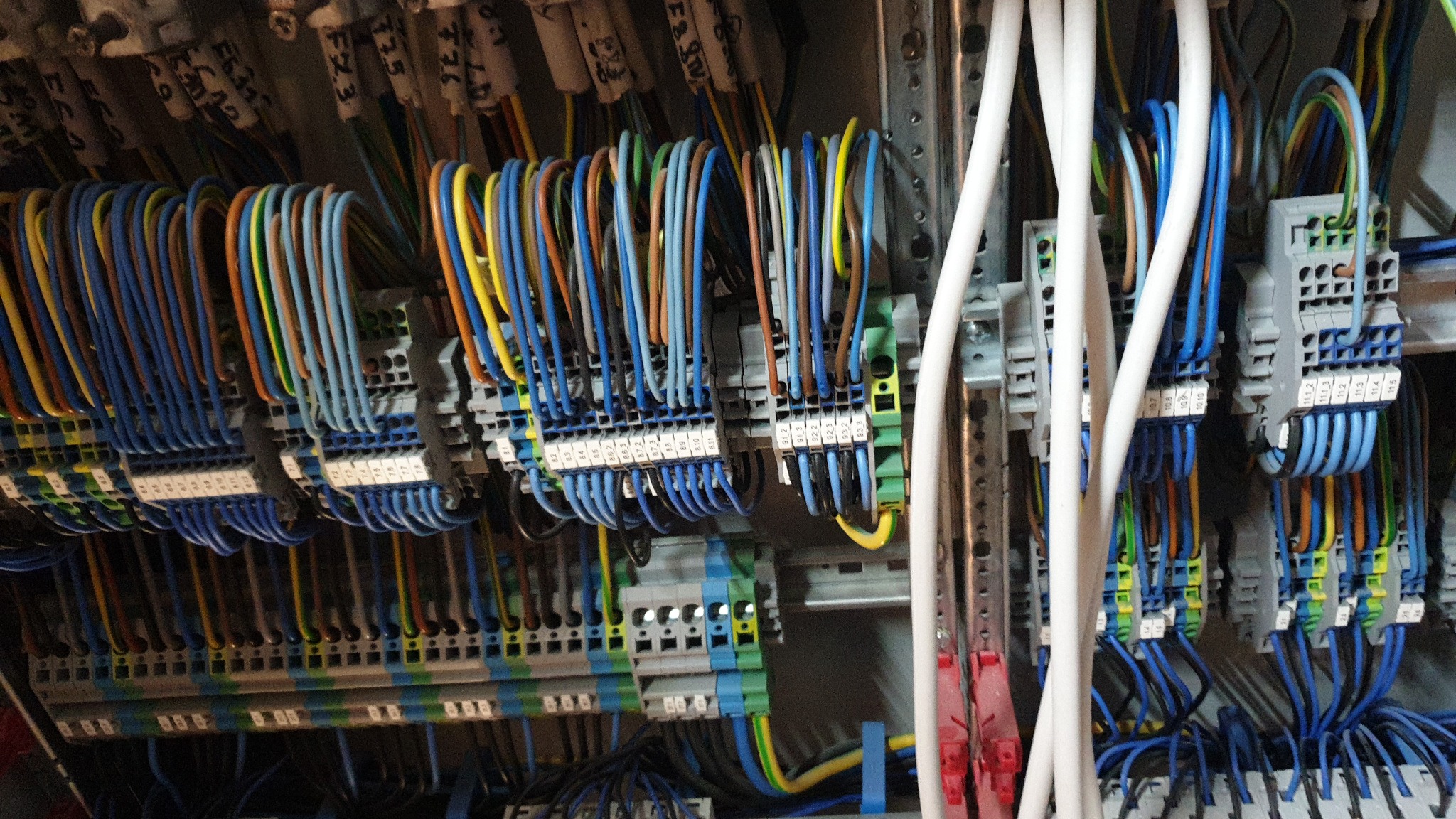 Panel elektryczny z uporządkowanymi przewodami w różnych kolorach, podłączonymi do listew zaciskowych z numerowanymi etykietami, widoczne szyny DIN.