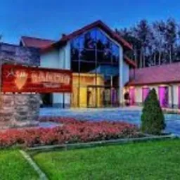 Elegancki budynek z aluminiową fasadą i szklanymi drzwiami wejściowymi w Opocznie, oświetlony wieczornym światłem, otoczony zadbanym trawnikiem i rabatami kwiatowymi.