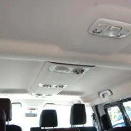 Wnętrze busa pasażerskiego: widok na sufit z oświetleniem i nawiewami, czarne zagłówki foteli w tle.