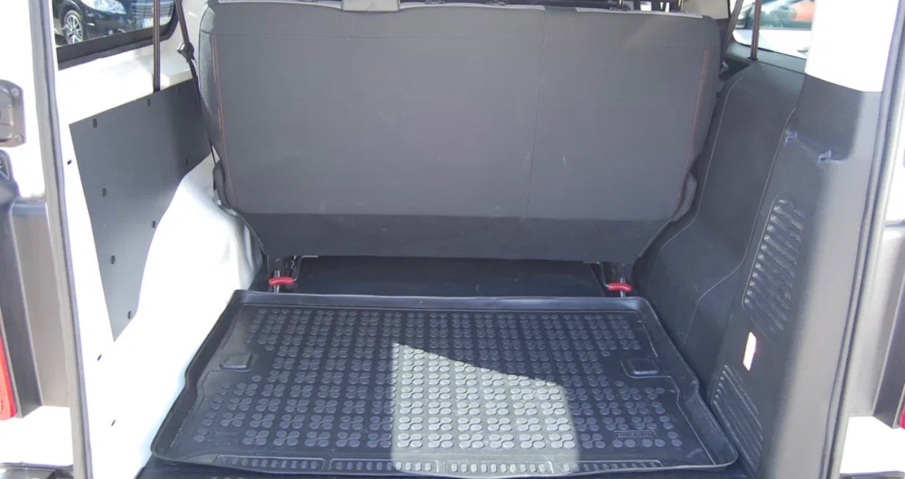 Wnętrze bagażnika białego samochodu dostawczego z rozłożonymi tylnymi siedzeniami i gumową wycieraczką podłogową z wzorem okręgów.