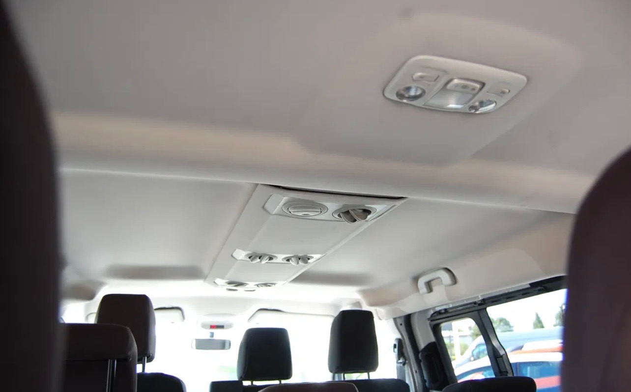 Wnętrze busa pasażerskiego: widok na sufit z oświetleniem i nawiewami, czarne zagłówki foteli w tle.