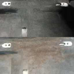 Częściowo wyczyszczona, szara tapicerka samochodowa z widocznymi mocowaniami foteli, ukazująca różnicę w wyglądzie przed i po czyszczeniu.