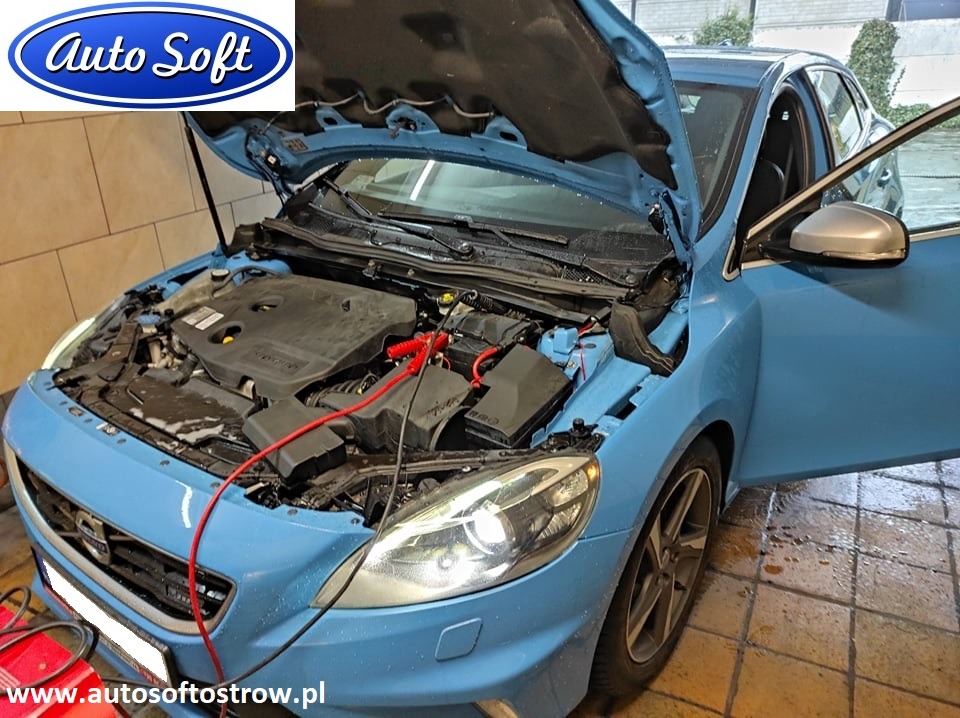 Niebieski samochód marki Ford z otwartą maską, podłączone kable rozruchowe, widoczne logo firmy Auto Soft w lewym górnym rogu i adres strony internetowej na dole zdjęcia.