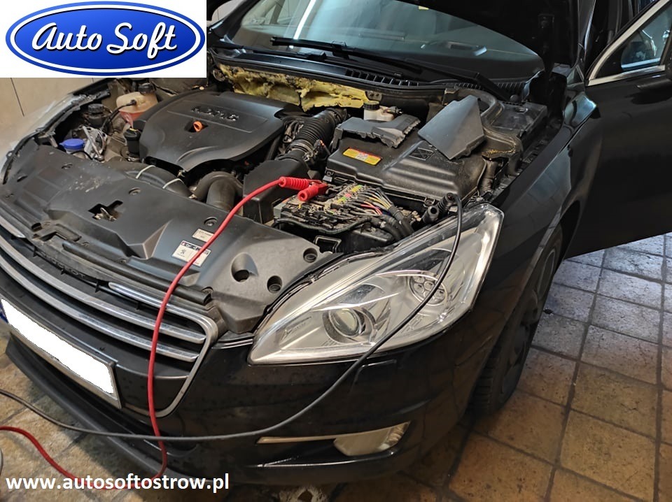 Czarny samochód z otwartą maską, widoczny silnik z podłączonymi przewodami diagnostycznymi, otwarte drzwi po stronie kierowcy.