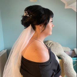 Malapert Beauty Studio - Profil kobiety z upiętymi ciemnymi włosami, welonem, ozdobną spinką z perełkami i błyszczącymi kolczykami, przygotowującej się do ślubu, na tle turkusowej ściany i pluszowego misia.