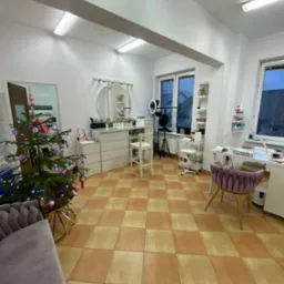 Wnętrze studia kosmetycznego z dwoma stanowiskami, jednym do manicure z fioletowym krzesłem i drugim do wizażu z lustrem, oświetleniem ring light i choinką w rogu pokoju.