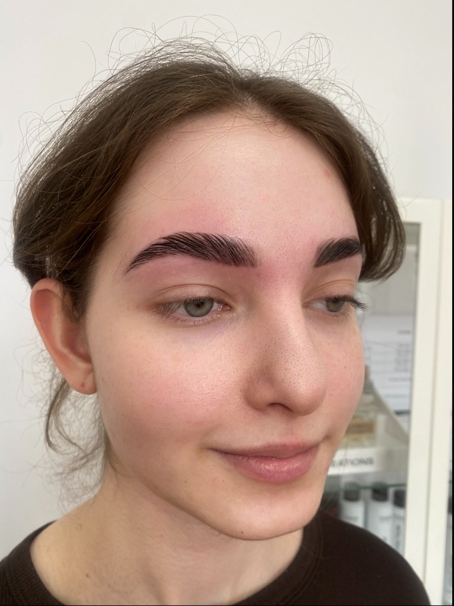 Młoda kobieta z ciemnymi, idealnie wystylizowanymi brwiami po zabiegu laminacji, z delikatnym uśmiechem i widocznymi drobnymi włoskami na czole.