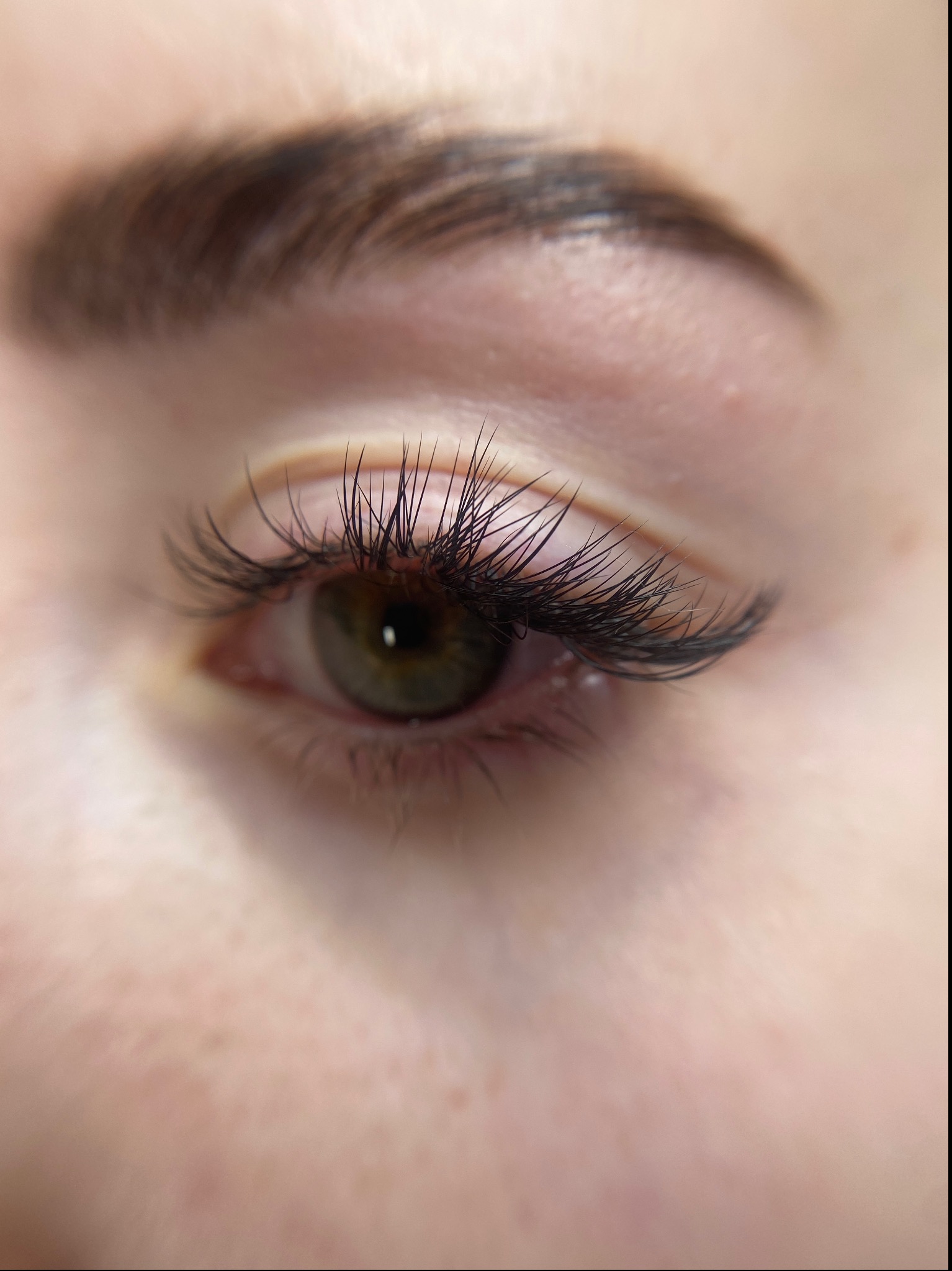 Zbliżenie na oko z zieloną tęczówką i wyraźnie przedłużonymi, czarnymi rzęsami. Widoczny fragment brwi.