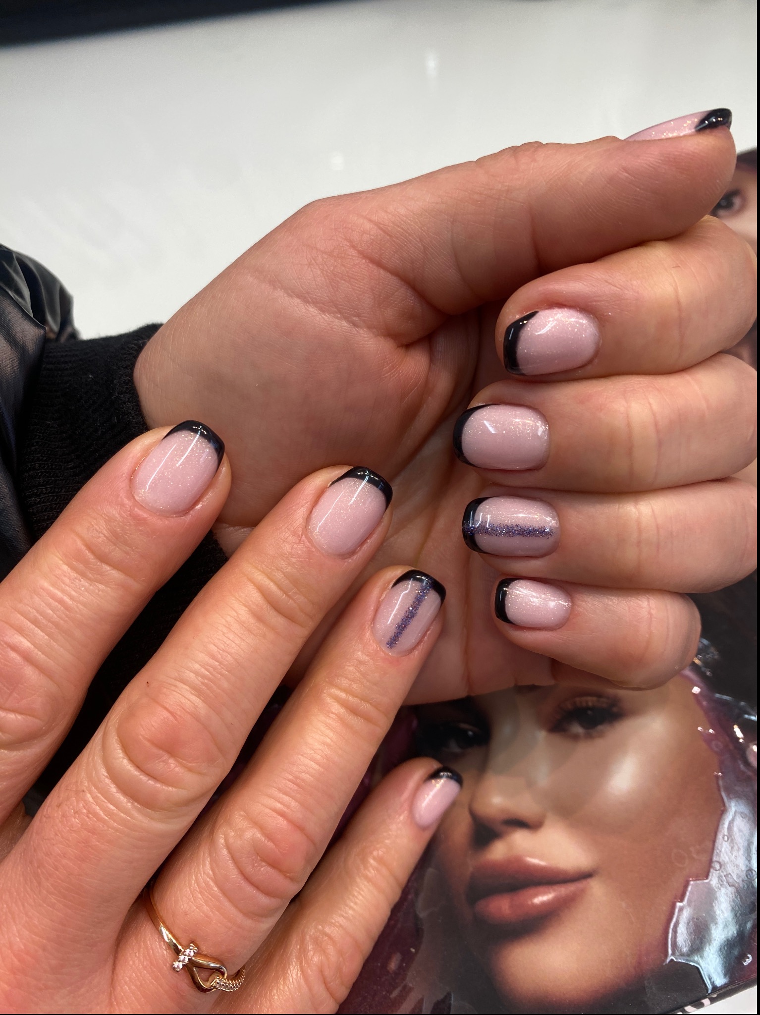 Dłonie z manicure hybrydowym: jasnoróżowa baza, czarny french i brokatowy pasek na jednym paznokciu, pierścionek na palcu