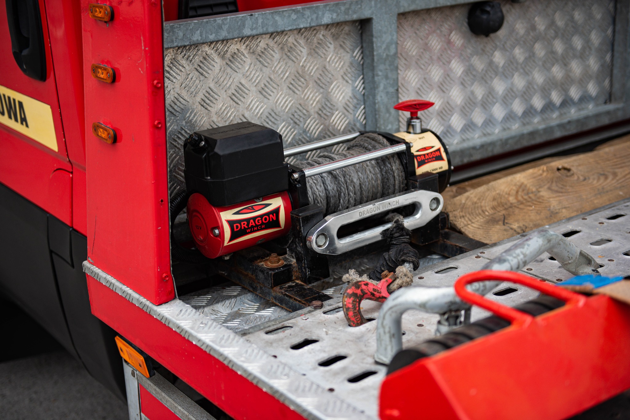 Czerwona laweta z zamontowaną wyciągarką Dragon Winch, widoczna stalowa platforma z kratownicą i elementami mocującymi.