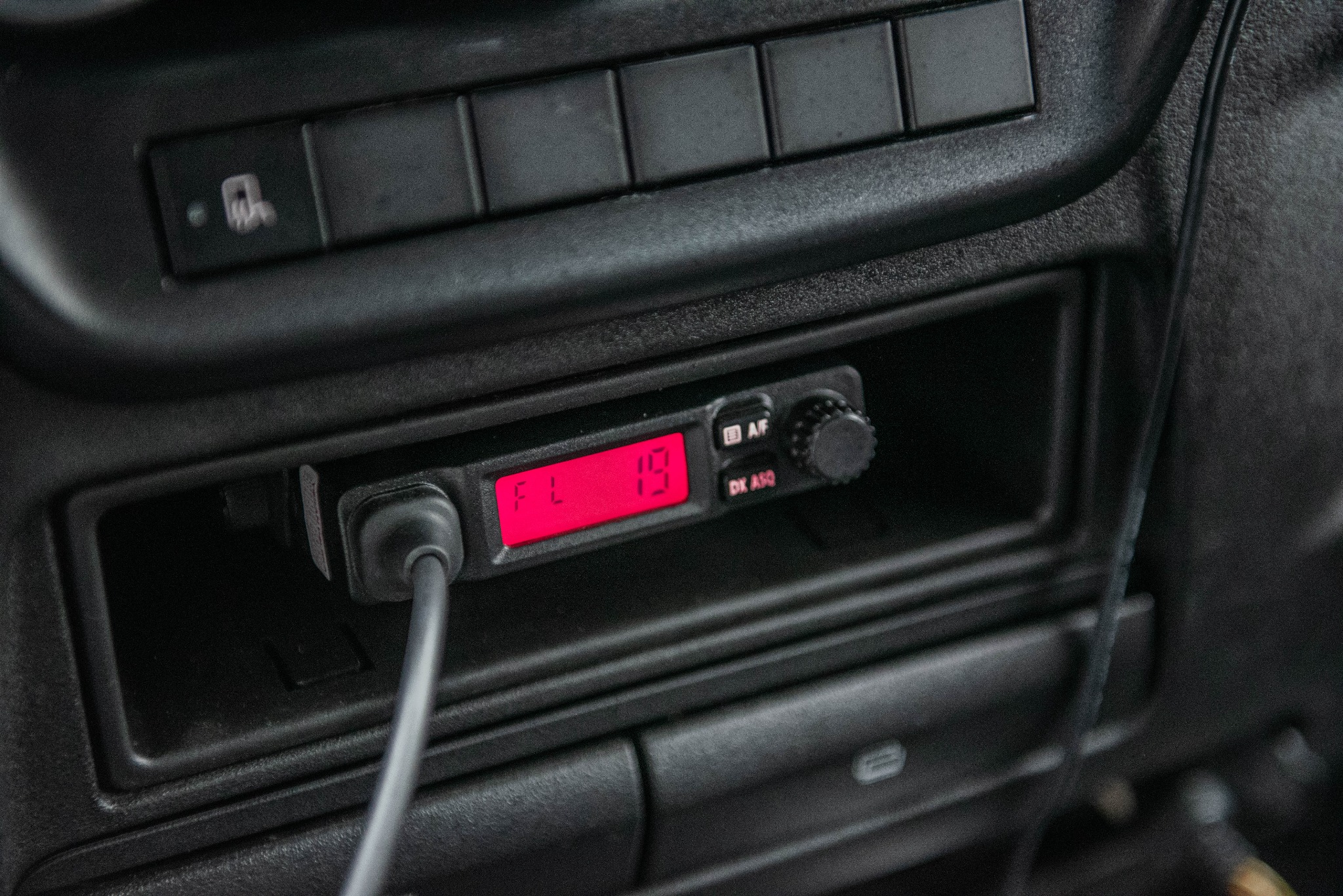 Czarny panel sterowania w kabinie pojazdu z zamontowanym radiem CB z czerwonym wyświetlaczem FL 19, widoczne przyciski i pokrętło regulacji.