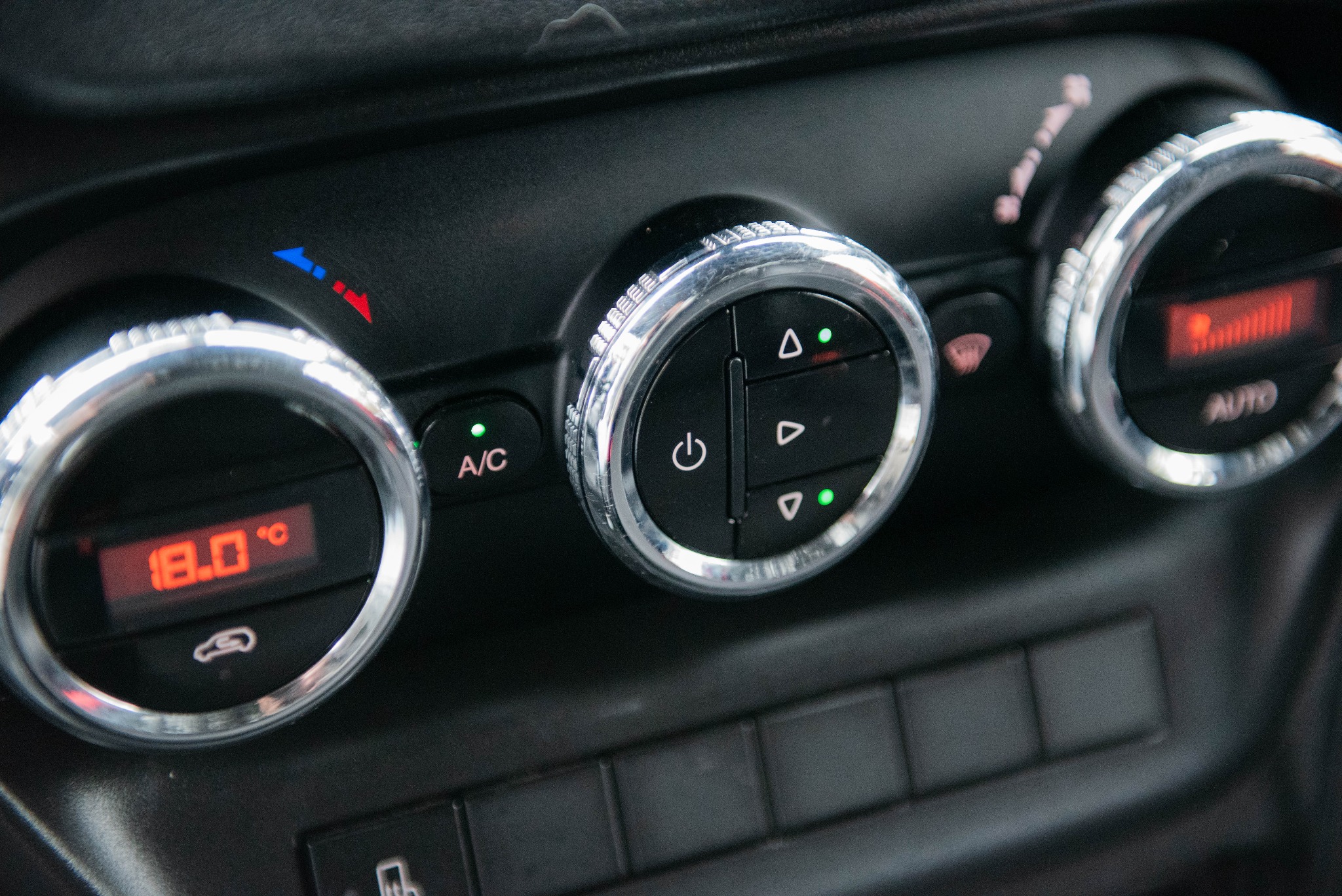 Panel sterowania klimatyzacją w samochodzie z Ostrowca Świętokrzyskiego, widoczne pokrętła z chromowanymi obwódkami i wyświetlacz temperatury.