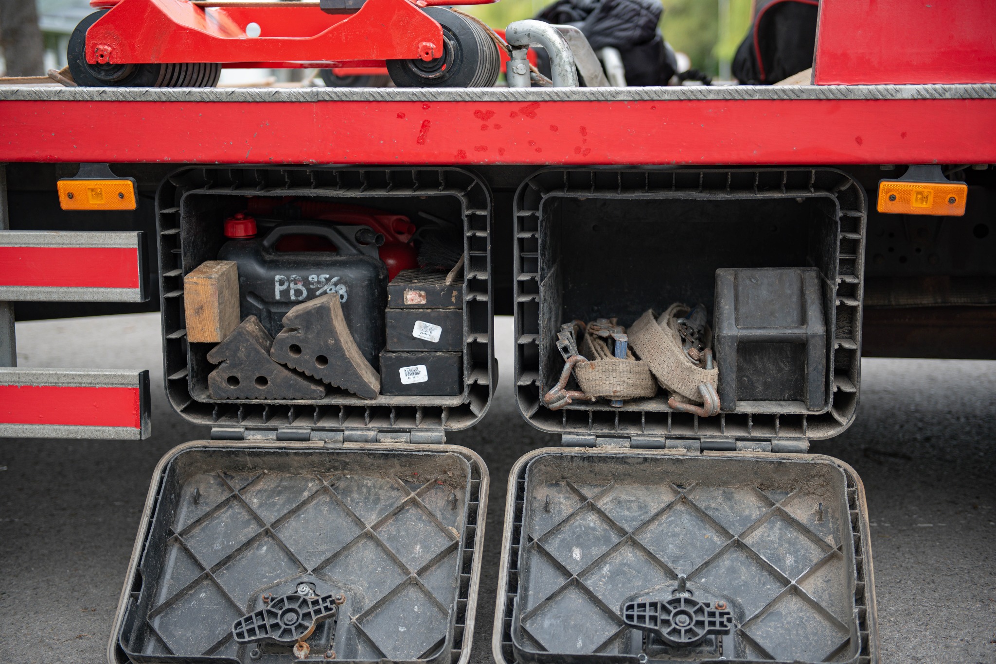 Otwarty schowek lawety z kanistrem, klinami pod koła, pasami transportowymi i innymi akcesoriami.