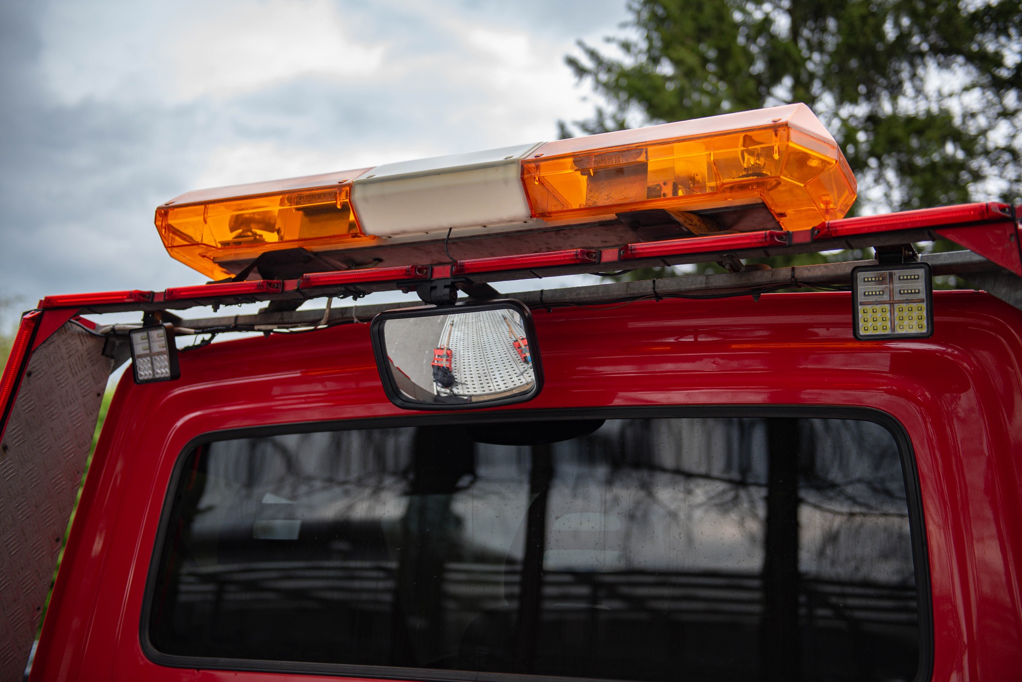 Czerwona laweta z pomarańczowym światłem ostrzegawczym i odbiciem przewożonego pojazdu w lusterku wstecznym.
