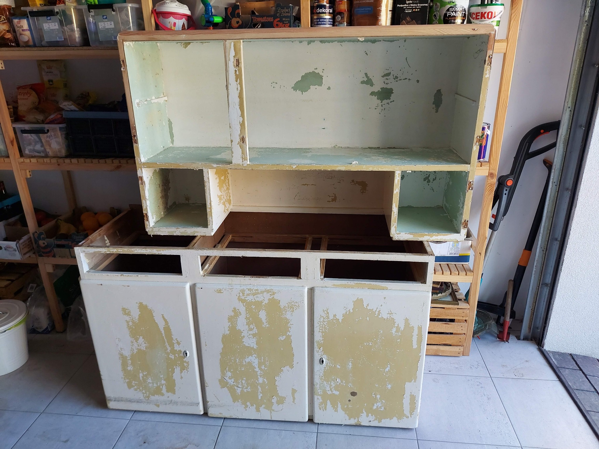 Demontaż starej, dwuczęściowej szafki z odłażącą farbą, przygotowanej do renowacji w garażu.
