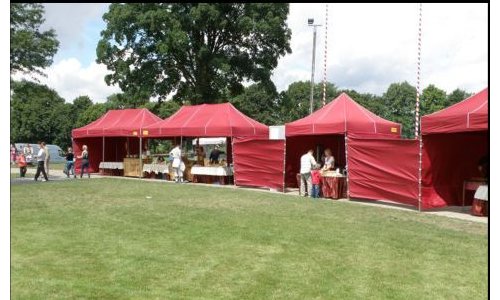 Rząd czerwonych namiotów z rozłożonymi stołami na trawiastym terenie, prawdopodobnie podczas imprezy plenerowej.