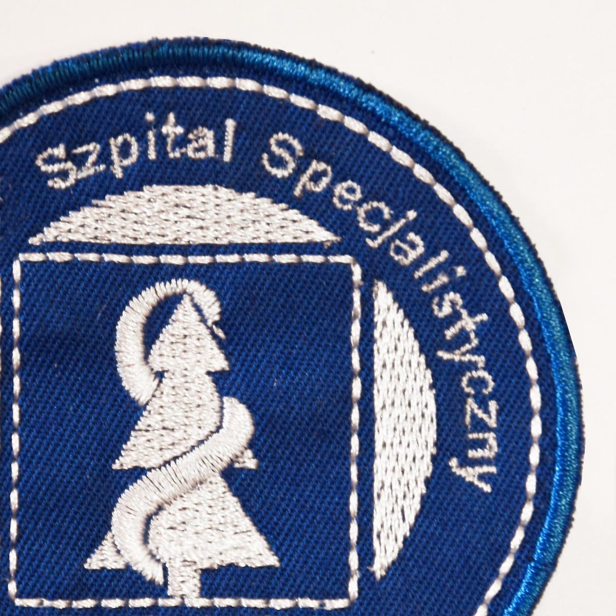 Fragment haftowanej naszywki Szpitala Specjalistycznego z symbolem Eskulapa na niebieskim tle.